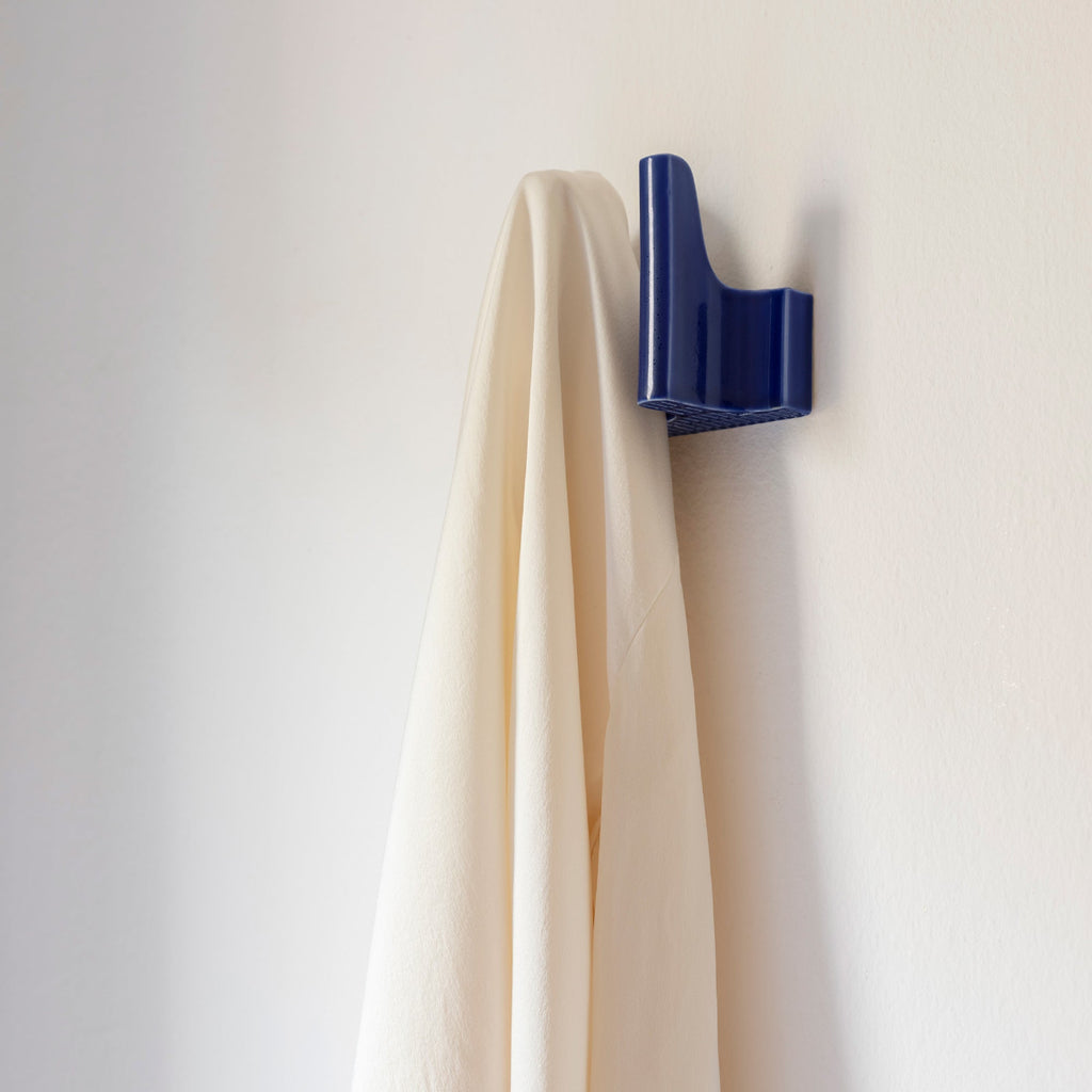 Interior view featuring a dark blue Tiili Wall Hook mounted on a wall, with a white collared shirt hanging from it.