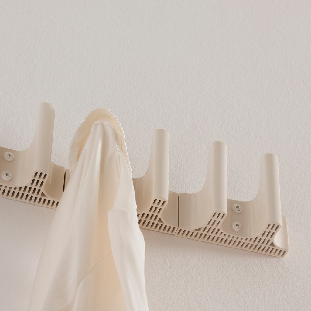 Interior view featuring three white Tiili Wall Hooks mounted side by side on a wall, with a white collared shirt hanging from one of the hooks.