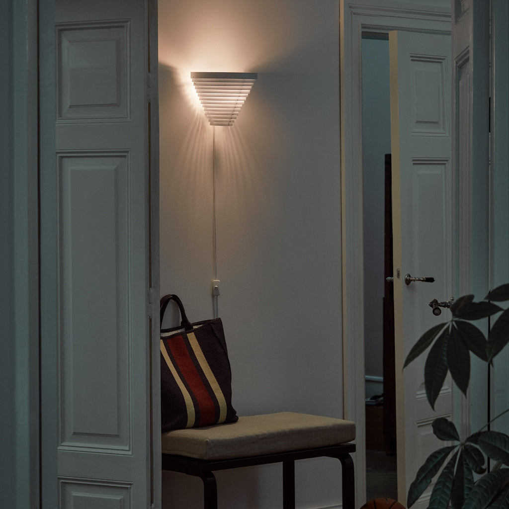 Interior view of a hallway featuring Wall Light A910 placed above Bench 153B, positioned between two doors. The light is switched on.